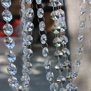 May include: Close-up of several strands of clear, faceted crystal beads. The beads are strung together with small silver-coloured rings, creating a shimmering, decorative effect. The crystals catch the light, reflecting multiple colours. Ideal for home decor or craft projects.