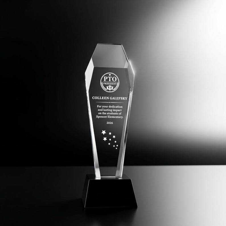 Op de afbeelding: Een heldere, taps toelopende glazen trofee met een zwarte voet. Het glas is gegraveerd met de tekst PTO PRESIDENT, COLLEEN GALEFSKY, For your dedication and lasting impact on the students of Spencer Elementary, 2026, en een groep sterren.