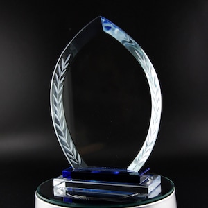 K&ouml;nnte beinhalten: Eine klare Glas-Troph&auml;e mit blauer Basis und einem Blattdesign. Die Troph&auml;e ist flammenf&ouml;rmig und hat einen leeren Platz zum Gravieren.