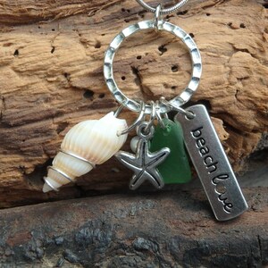 May include: A silver necklace with a charm circle, a seashell, a starfish, a piece of green sea glass, and a silver tag that says "beach love".
