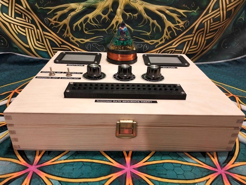 May include: A wooden box with a complex control panel featuring knobs, switches, and digital displays. A glass dome with a decorative element sits atop the box. The text "RADIONIC RATE SEQUENCE INSERT" is visible.