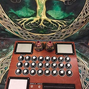 Può includere: Un dispositivo elettronico in legno con numerosi pulsanti e quadranti, etichettato "Input Plate" e "Out Plate". Due oggetti decorativi sono posti sopra il dispositivo. Lo sfondo presenta un arazzo con un disegno dell'albero della vita.