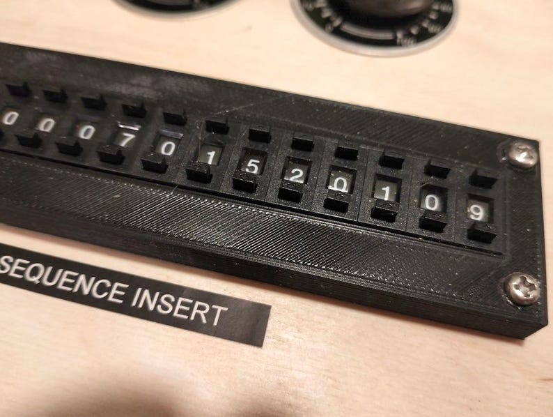 May include: A black sequence insert with white numbers and the text "SEQUENCE INSERT". The insert has a series of rotating number dials from 0 to 9. The insert is secured with two screws.