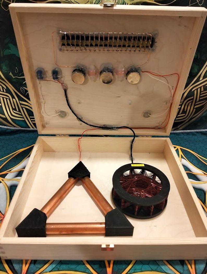 May include: Open wooden box with electronic components. Inside, a copper triangle, a coil of wire, and various circuits are visible. The box is open, revealing the internal wiring and components.