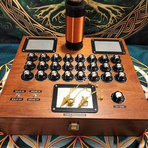 May include: A wooden box with a control panel featuring numerous knobs, switches, and a tuning sensor plate. A copper coil and a silver sphere are on top. The text "SCALAR ON", "ORGONE ON", "SCALAR OFF", and "ORGONE OFF" are visible.