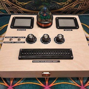 May include: A wooden radionics device with two rectangular input/output plates, knobs, switches, and a sequence insert. The device has the text "INPUT PLATE", "OUT PLATE", "ORGONITE ON", "VORTEX ON", "ORGONITE OFF", "VORTEX OFF", and "RADIONIC RATE SEQUENCE INSERT". A decorative glass object sits on top.
