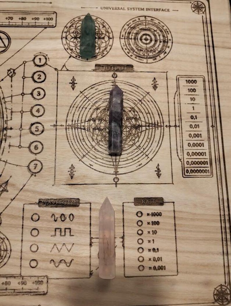 May include: A wooden board with etched geometric designs and text, including "UNIVERSAL SYSTEM INTERFACE" and numerical scales. Three crystal points in green, purple, and pink are arranged on the board, suggesting a spiritual or metaphysical theme.