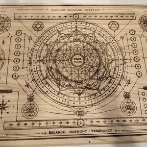 May include: A wooden board with a complex geometric design, featuring circles, lines, and text. The text includes "RADIONIC MACHINE INTERFACE", "STICK PLATE", and scales with numbers. The design is etched into the light-colored wood, creating a detailed, technical aesthetic.