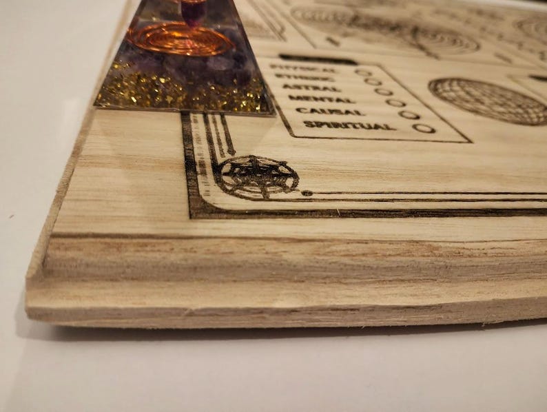May include: A wooden board with etched designs and text, including a pyramid-shaped object with purple and gold accents. The board features geometric patterns and the words "PHYSICAL", "ASTRAL", "MENTAL", "CAUSAL", and "SPIRITUAL".