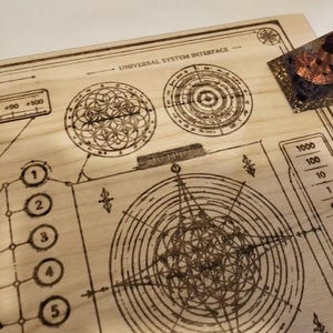 May include: A wooden board with etched geometric designs and the text "UNIVERSAL SYSTEM INTERFACE." A small, triangular object with copper coils and a dark purple base sits on the board. The board features circular patterns, lines, and numbers.