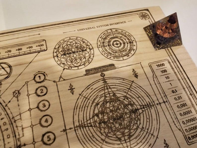 May include: A wooden board with etched geometric designs and the text "UNIVERSAL SYSTEM INTERFACE." A small, triangular object with copper coils and a dark purple base sits on the board. The board features circular patterns, lines, and numbers.