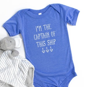 May include: A blue baby onesie with the text "I'm the captain of this ship" and three anchor symbols. A gray elephant stuffed animal with a white and gray patterned blanket is in the foreground.