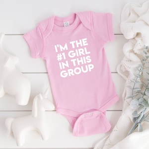 May include: Pink baby onesie with white text that reads "I'm the #1 girl in this group".