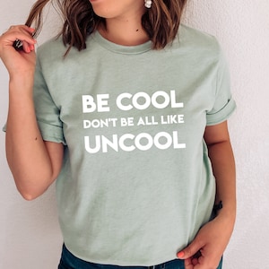 Puede incluir: Una camiseta verde claro con el texto "BE COOL DON'T BE ALL LIKE UNCOOL" impreso en blanco.