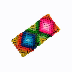 Puede incluir: Una pinza para el pelo rectangular de colores con un patrón geométrico de cuadrados en tonos de rosa, azul, verde, amarillo, naranja y rojo.