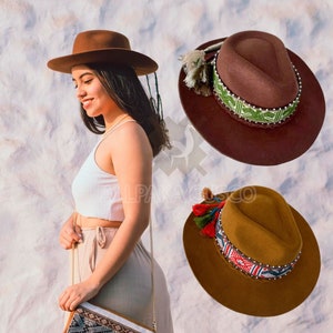 Puede incluir: Tres sombreros fedora de fieltro marrón con bandas tejidas de colores y borlas. Los sombreros tienen un ala ancha y una forma clásica de fedora.