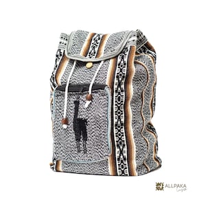 May include: A woven fabric backpack featuring a black, white, and brown striped pattern with a central llama silhouette on the front pocket. The bag includes a flap closure with a wooden button, white drawstring cords, and the text ALLPAKA Cusco.