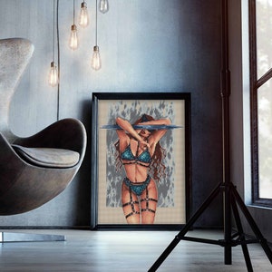 Peut inclure: Une œuvre d'art encadrée représentant une personne pixelisée en lingerie turquoise avec des lanières noires. L'œuvre est dans un cadre noir, appuyée contre un mur gris. La pièce comprend une chaise moderne et des ampoules suspendues.