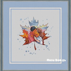 May include: Cross-stitch artwork in a blue wooden frame. The image shows a couple embracing behind a large, orange and red maple leaf. The background depicts a sunset. The text "Mila Vod'd" is in the bottom right corner of the artwork.