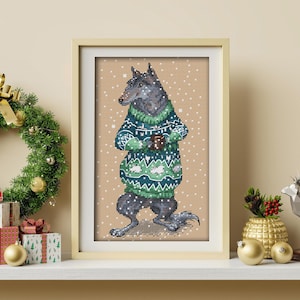 Puede incluir: Un diseño de punto de cruz enmarcado de un lobo con un suéter navideño verde y azul con un patrón de copo de nieve. El lobo está de pie sobre un fondo marrón con copos de nieve blancos.