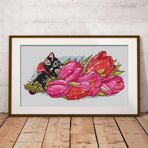 May include: Cross-stitch art of a black cat nestled among pink and red tulips. The cat has green eyes and is wearing a red bow. The artwork is framed in a brown wooden frame and set against a white background.