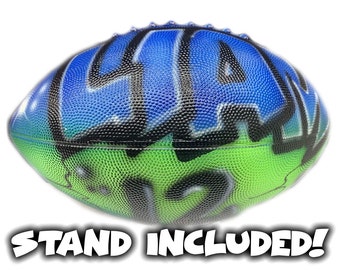 May include: A blue and green football with black graffiti-style lettering. The football has a stand included.