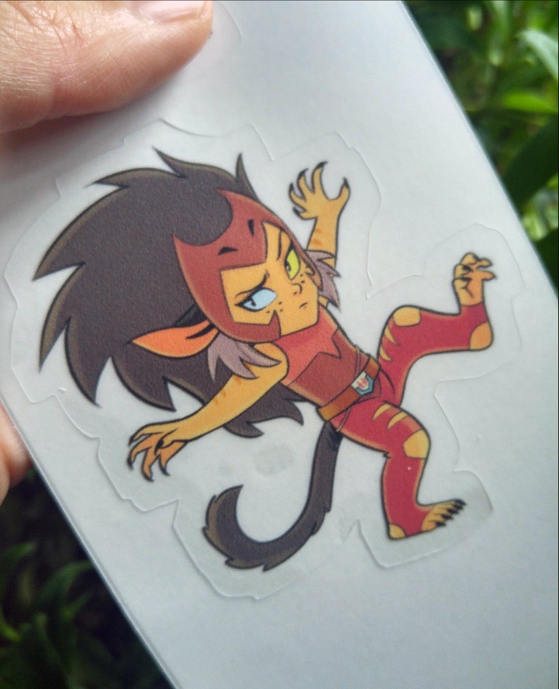 May include: A cartoon sticker of a red and yellow lion-like character with a black mane, wearing a red and brown outfit. The character is in a dynamic pose with one leg raised and claws extended.