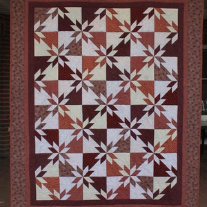 Peut inclure: Une courtepointe avec un motif géométrique de triangles bruns, blancs et orange. La courtepointe est composée de nombreux petits carrés, chacun avec un motif différent.