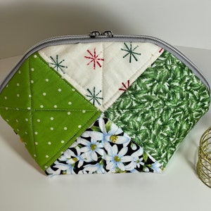 May include: A green and white quilted makeup bag with a zipper closure. The bag is made of different patterned fabrics, including green polka dots, white with red and green snowflakes, green leaves, and white flowers on a black background.
