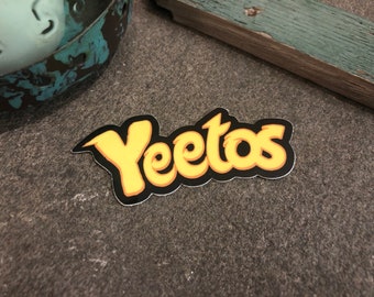 May include: A yellow sticker with the word "Yeetos" written in a stylised font on a black background.