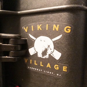May include: A white sticker with a skull and crossbones design. The text "VIKING VILLAGE" is in yellow above the skull and "BARNEGAT LIGHT, NJ" is in yellow below the skull.