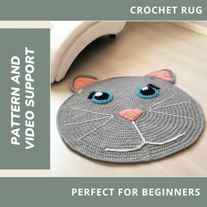 Puede incluir: Una alfombra de ganchillo gris hecha a mano con forma de cara de gato. La alfombra presenta ojos azules, una nariz rosa y bigotes blancos. Las orejas son grises con detalles en rosa y naranja. El texto en la imagen dice "CROCHET RUG" y "PATTERN AND VIDEO SUPPORT".