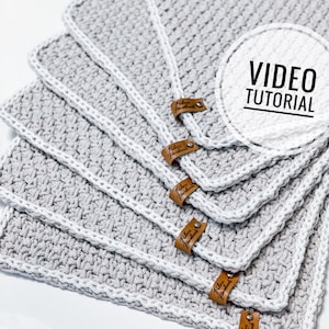 Puede incluir: Seis cuadrados de crochet grises con bordes blancos y etiquetas de cuero marrón que dicen "Robin Handmade". Los cuadrados están apilados uno encima del otro. La imagen incluye el texto "VIDEO TUTORIAL".