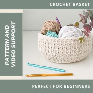 May include: A cream-colored crochet basket filled with yarn in various colors. Two crochet hooks, one blue and one gold, are in front of the basket. Text at the top reads "CROCHET BASKET" and at the bottom "PERFECT FOR BEGINNERS".