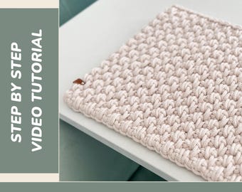 Peut inclure: Un dessous de plat au crochet beige avec une surface texturée. L'image comprend le texte "CROCHET PLACEMAT" en haut et "STEP BY STEP VIDEO TUTORIAL" sur le côté gauche. Une petite étiquette marron est attachée au dessous de plat.