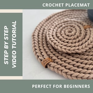 Può includere: Primo piano di un sottobicchiere all'uncinetto beige con un motivo a spirale. Il sottobicchiere è realizzato con filato spesso e intrecciato. Il testo "CROCHET PLACEMAT" e "STEP BY STEP VIDEO TUTORIAL" sono visibili. Il testo "PERFECT FOR BEGINNERS" è visibile.