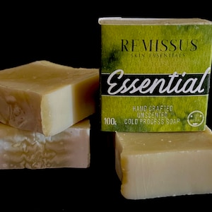 Könnte beinhalten: Vier Stück handgemachte, unparfümierte, kaltgepresste Seife. Die Seife ist hellbeige und hat ein natürliches, erdiges Aussehen. Die Verpackung ist grün mit dem Text "Remissus Skin Essentials Essential 100g Cold Process Soap" darauf gedruckt.