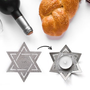 May include: Two silver Star of David candle holders, one with a white tea light candle inside. The candle holder is designed to be folded into a three-dimensional shape.
