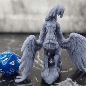 May include: A gray 3D printed miniature of a winged humanoid creature with a bird-like head and outstretched wings. The miniature is standing on a base and is posed with its head tilted back.