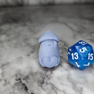 May include: A blue and white ceramic mushroom figurine next to a blue iridescent dice with white numbers 13, 5, and 15.