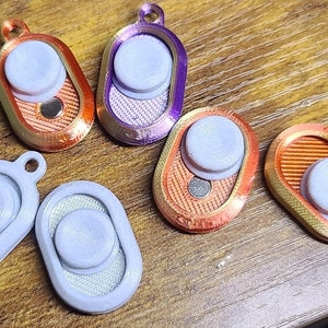 May include: Five different colored phone grips with a white button. The grips are oval shaped and have a textured surface.
