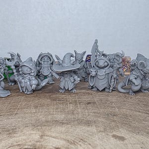 May include: A collection of gray fantasy miniatures, including wizards, creatures, and a mouse-like figure, are arranged on a wooden surface. Several multi-sided dice are also present. The miniatures are detailed and appear to be 3D-printed.
