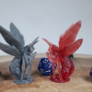 May include: Two miniature figurines of insects with wings. One is gray and the other is red. Both are standing on a wooden surface with dice.