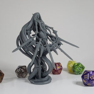 May include: A gray 3D printed miniature of a female figure with long flowing hair and multiple swords. The figure is standing on a round base. There are several colorful dice scattered around the figure.