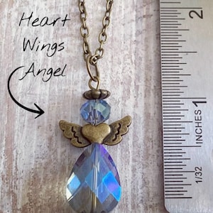 May include: A bronze-toned necklace featuring a pendant in the shape of an angel. The angel has a heart-shaped body, small wings, and a large, iridescent teardrop-shaped crystal. The text "Heart Wings Angel" is written on the left side of the image.