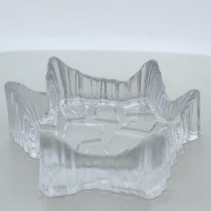 May include: Clear glass star-shaped dish with a textured, rough exterior. The interior features a mosaic-like pattern. The dish is designed with raised edges and a shallow bowl, perfect for decorative use.