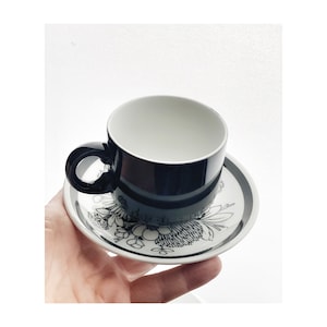 Könnte beinhalten: Ein schwarzes und weißes Blumen-Teetassen-Set. Die Untertasse hat einen schwarzen Rand und eine weiße Mitte mit einem schwarzen Blumendesign. Die Teetasse ist schwarz mit einem weißen Innenraum.