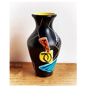 Può includere: Vaso in ceramica nera con bordo giallo e disegni astratti colorati. Il vaso è decorato con vernice nera, bianca, gialla, arancione e blu.