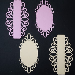 May include: Three decorative paper frames with intricate cut-out designs. Two frames are oval shaped with a pink and beige background. One frame is rectangular with a pink and beige background.