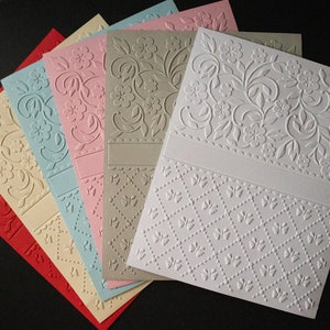 May include: Six embossed cardstock sheets in various colours, including red, beige, light blue, pink, grey, and white. Each sheet features a different embossed design, including floral patterns and a geometric pattern.